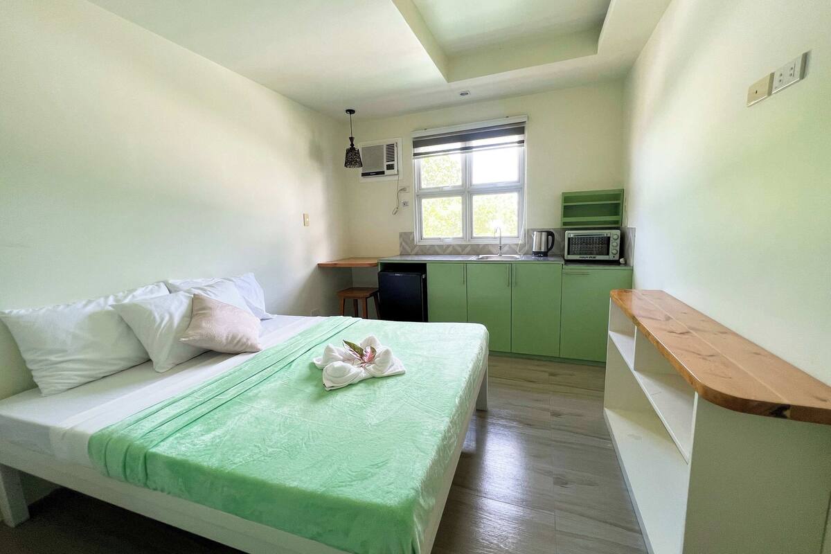 Habitación pequeña con cama, kitchenette y ventana.