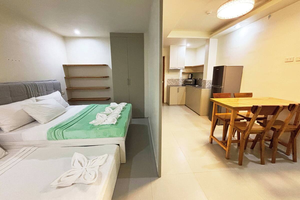 Habitación de hotel con dos camas, una kitchenette pequeña y un comedor con mesa y sillas.