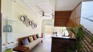 Un espace de vie moderne avec un canapé en bois, des étagères blanches, des œuvres d’art décoratives au mur, un ventilateur de plafond et un escalier avec une rampe en bois.