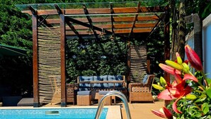 A poolside area with a wooden pergola, wicker furniture, and a clear blue pool.