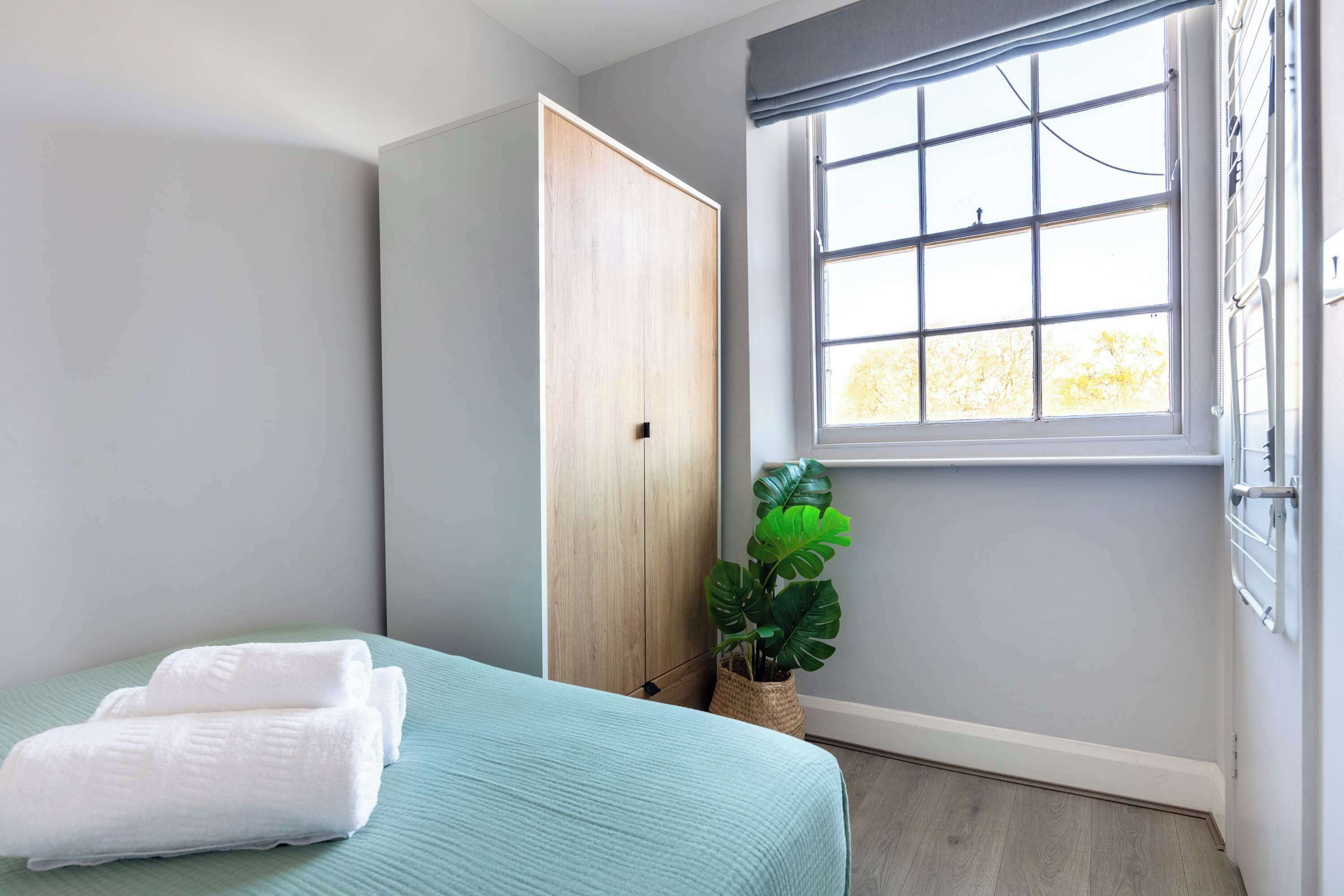 Quarto com cama, guarda-roupa, janela e uma planta.