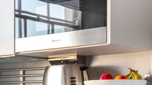 A kitchen with a stainless steel microwave, a coffee maker, a kettle, and a bowl of fruit on a shelf. - Cosy 1BR Steps from Camden Market & Regent's Park (London)