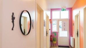 A hallway with a mirror, a door with emergency exit signs, and a fire extinguisher. - Hostel Fjordur (Hafnarfjörður)
