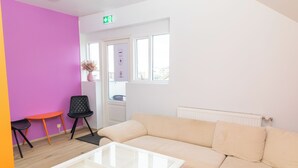 A room with a beige sofa, a glass coffee table, a black chair, and a small orange table. - Hostel Fjordur (Hafnarfjörður)