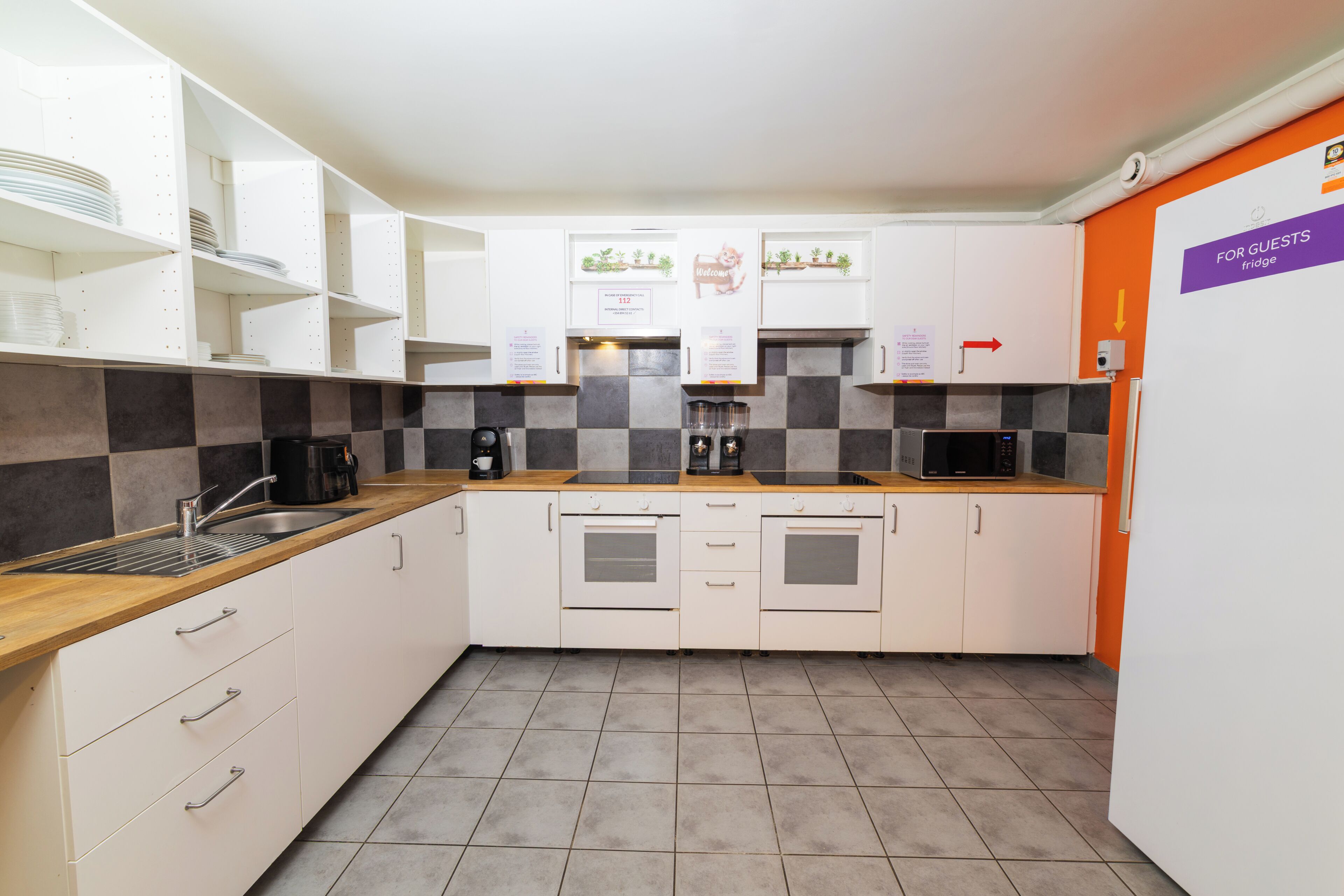 A modern kitchen with white cabinets, a checkered backsplash, and a 'For Guests' fridge sign.