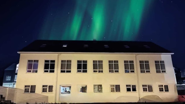 A building with multiple windows and a flat roof, under a night sky with green aurora lights. - Hostel Fjordur (Hafnarfjörður)