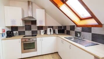 A kitchen with white cabinets, a stainless steel oven, a microwave, a coffee maker, and a sink with a window above.