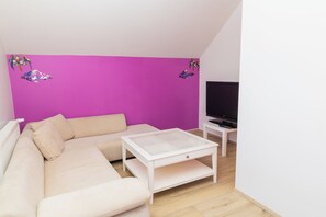 A modern living room with a beige sofa, a white coffee table, and a flat-screen TV on a white stand. - Hostel Fjordur (Hafnarfjörður)