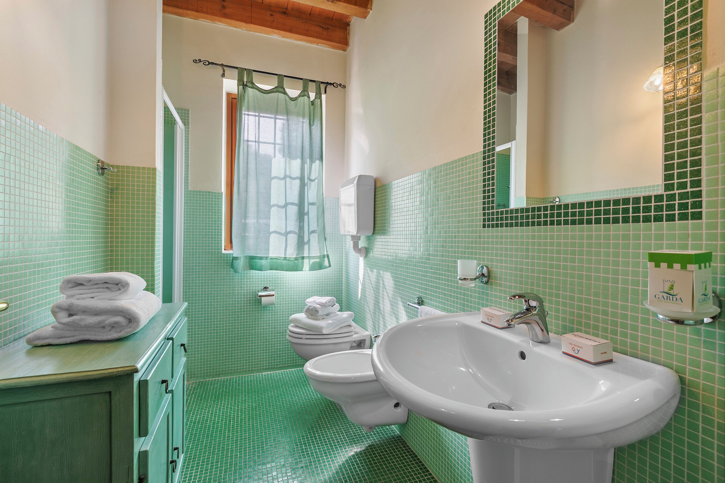 A bathroom with green tiled walls, a sink, a mirror, and a toilet.