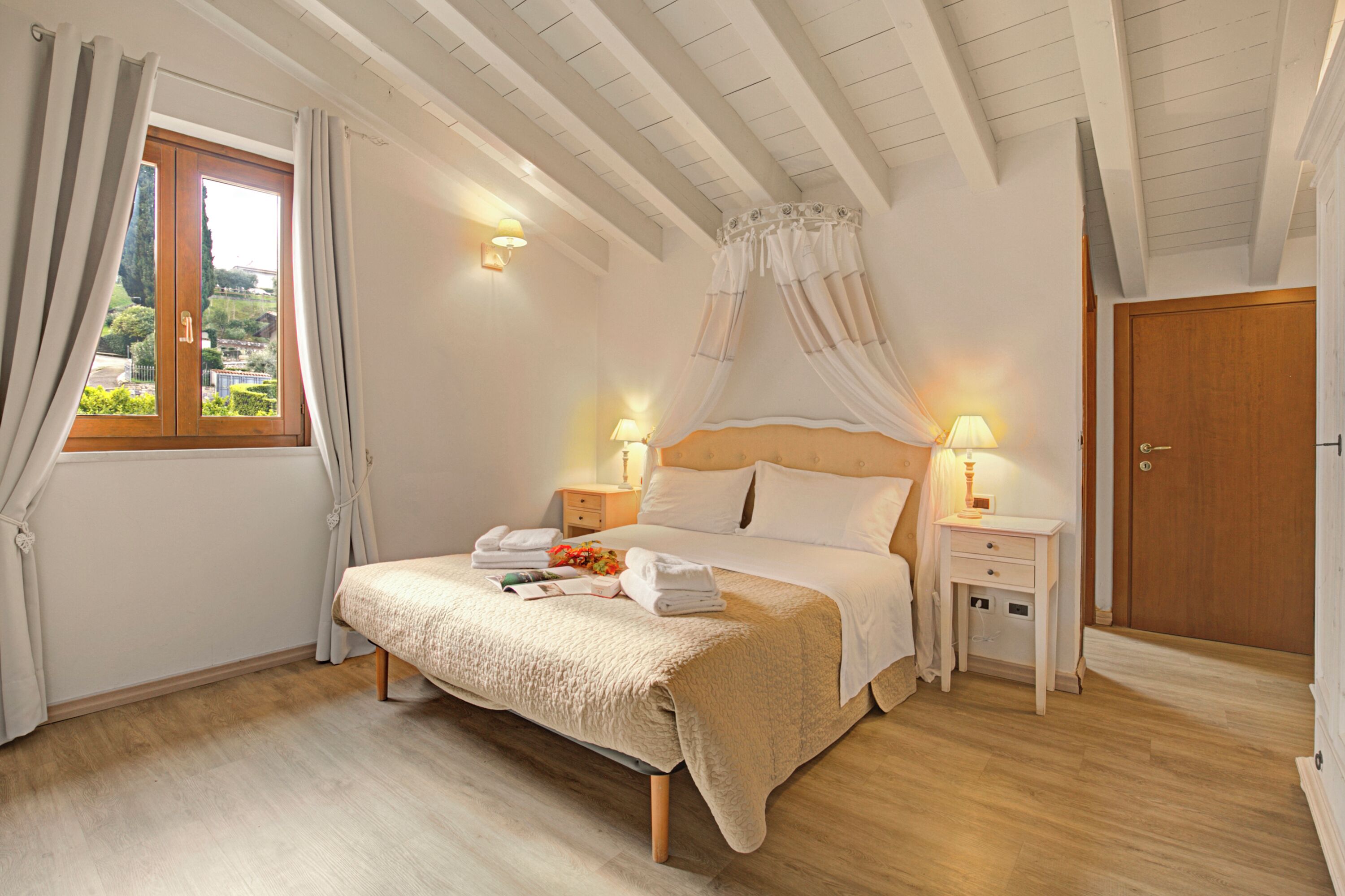 A bedroom with a bed, bedside tables, a window with curtains, and a view of the outside.