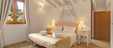 A bedroom with a bed, bedside tables, a window with curtains, and a view of the outside.