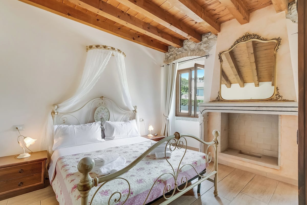 Un dormitorio con una cama con dosel, una chimenea de piedra y vistas al exterior.