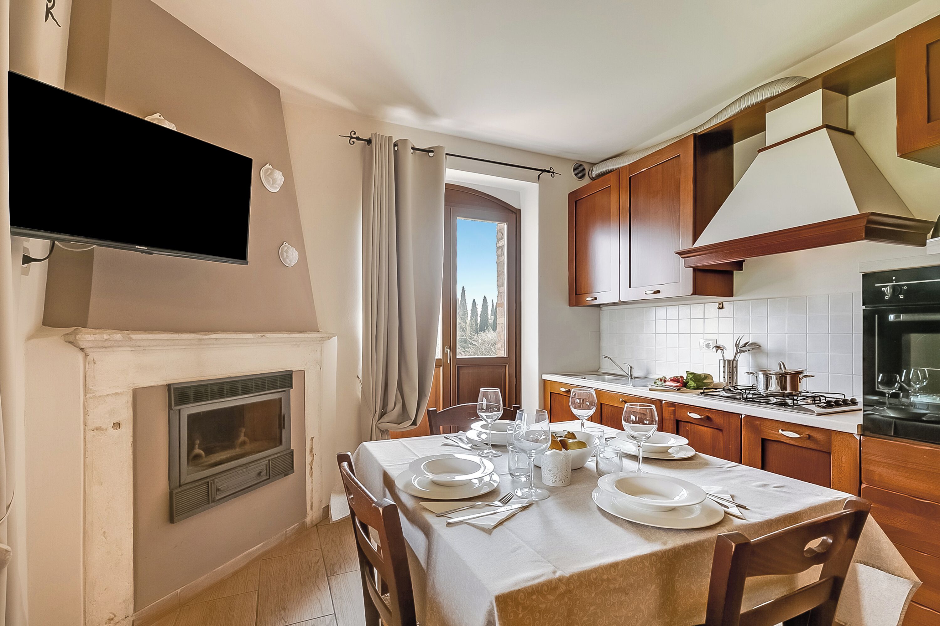 A dining area with a fireplace, a television, and a kitchen with wooden cabinets and a stove.