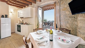 Un coin repas avec une table dressée pour deux personnes, une bouteille de vin et une vue sur l’extérieur par une porte ouverte.