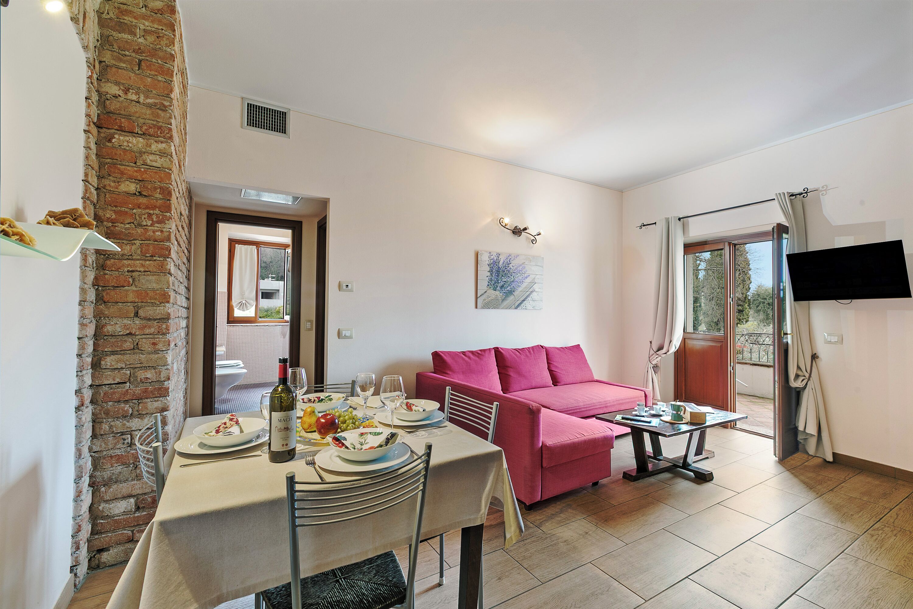 A dining area with a table set for four, a pink sofa, and a TV mounted on the wall.