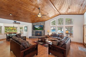 Un salón amplio con chimenea de piedra, techo de madera y ventanas grandes que ofrecen vistas al exterior.