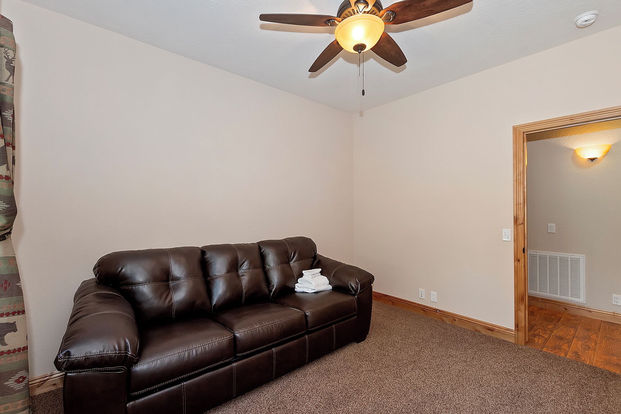 Une pièce avec un canapé en cuir marron, un ventilateur de plafond et une porte dotée d’un luminaire.