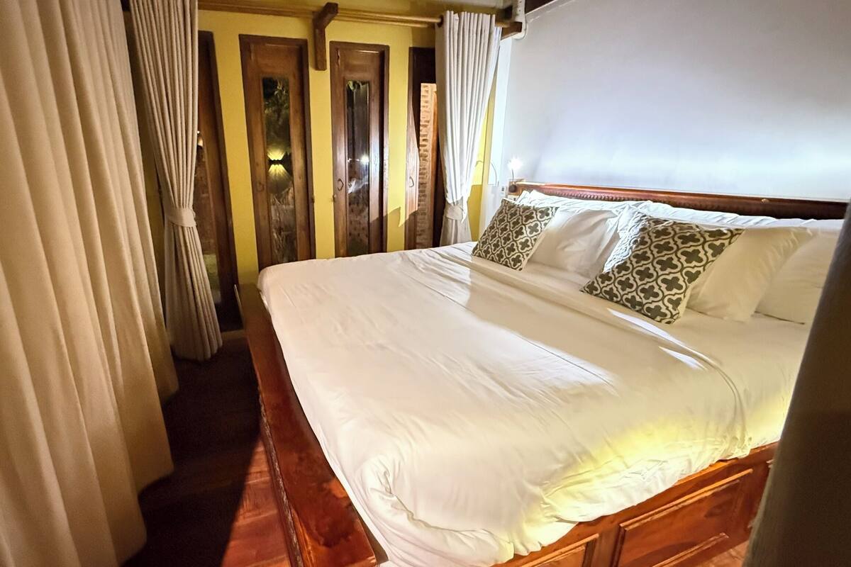 A hotel room with a large bed, wooden headboard, and curtains.