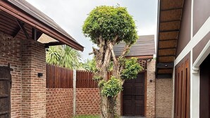 A courtyard with a brick building, a tiled patio, and a tree. - Kawarin Kanpuri Villas (Kanchanaburi)