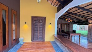 A wooden door with a decorative design, a bench, and a table under a covered area with a tiled floor. - Kawarin Kanpuri Villas (Kanchanaburi)