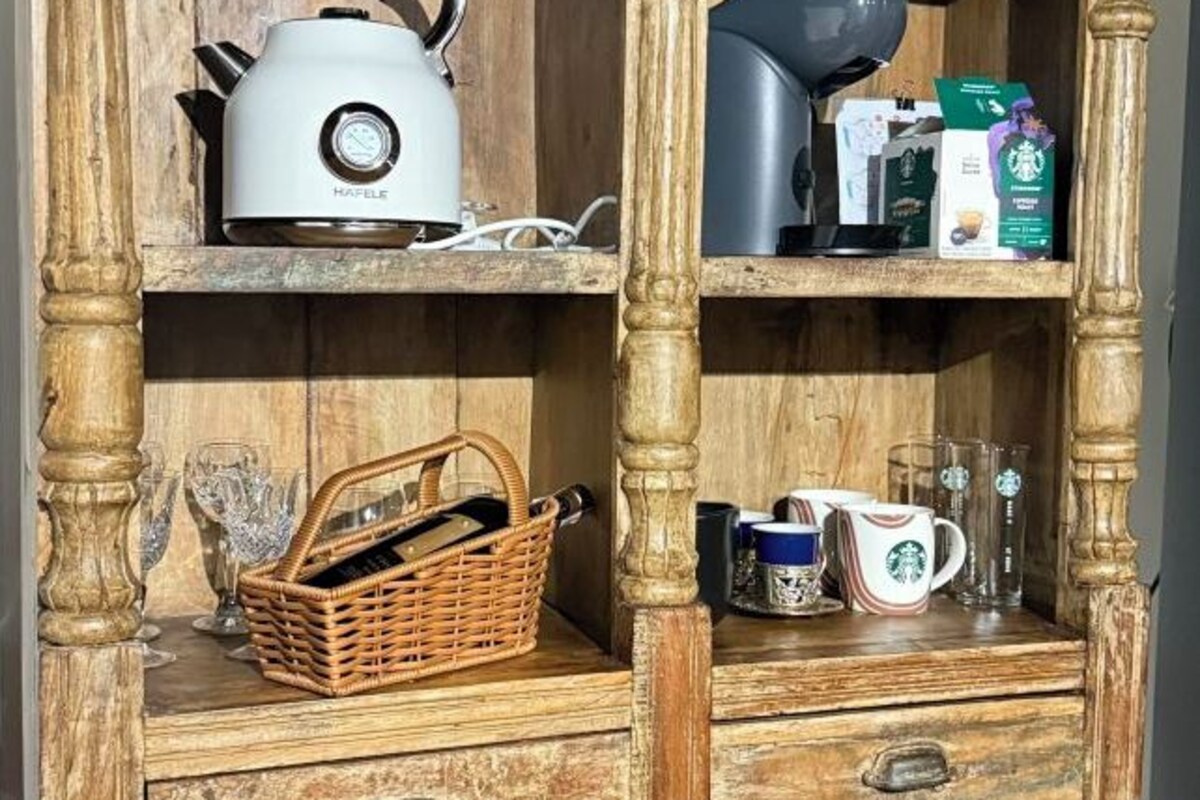 A wooden shelf with a white kettle, a basket, and a drawer with a coffee maker and Starbucks cups.