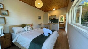 Un dormitorio con techo de madera, una cama con ropa blanca, un plaid verde y una mesita de noche con lámpara.