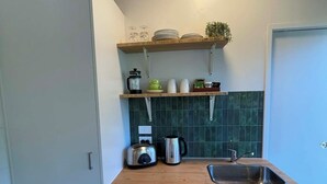 Una cocina compacta con armarios blancos, encimera de madera, pileta y salpicadero verde.