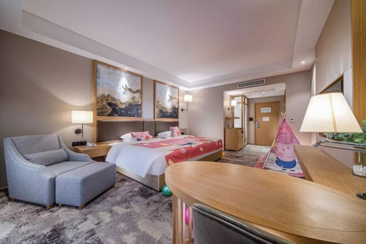 Quarto de hotel com cama, sofá, escrivaninha e obras de arte nas paredes.