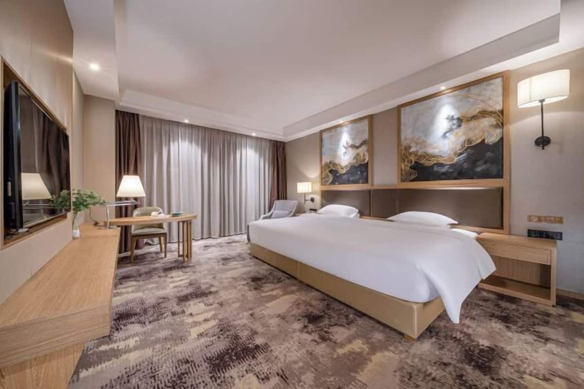 Quarto de hotel com uma cama grande, uma escrivaninha, uma cadeira, televisão e obras de arte nas paredes.