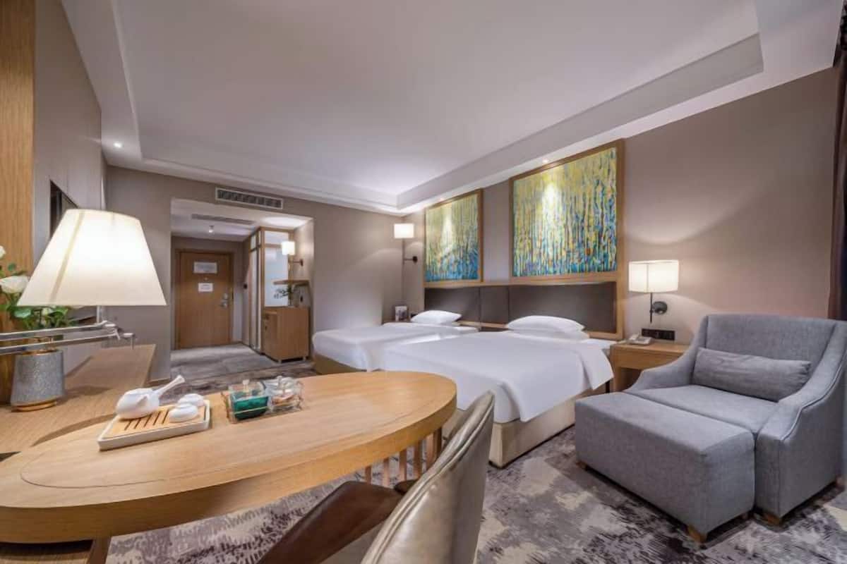 Quarto de hotel com cama, escrivaninha, cadeira e obras de arte na parede.