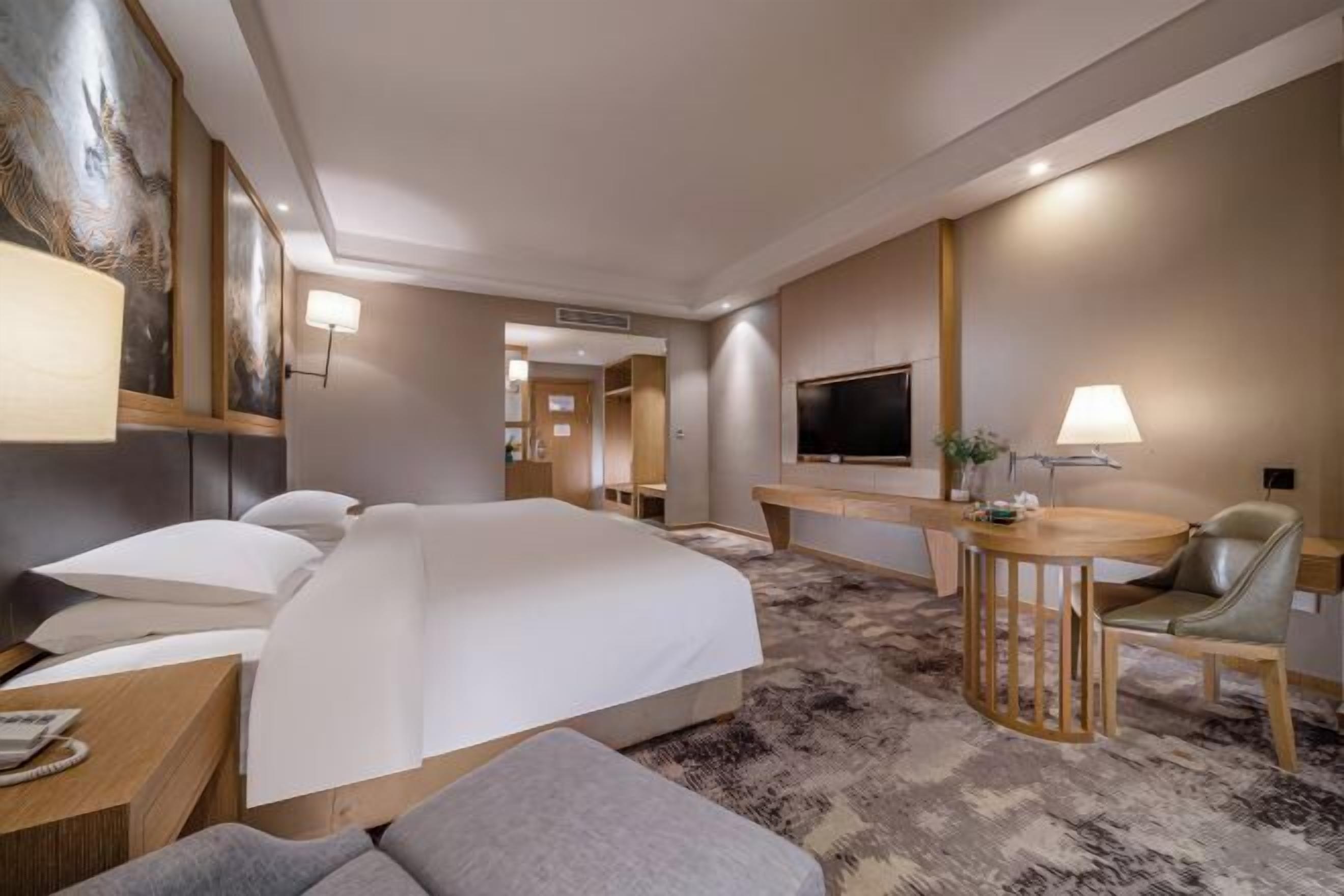 A hotel room with a large bed, a desk with a chair, a television, and a wall-mounted artwork.