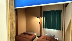 A compact room with two single beds, a bedside table, a lamp, and a curtain. - Backpackers Jinya (Takayama)