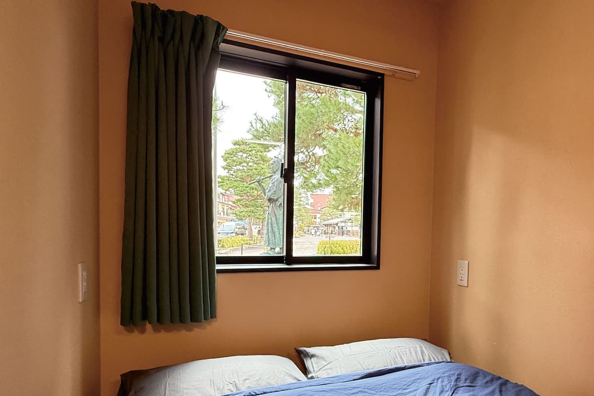 Ein Zimmer mit einem Bett, einem Fenster mit Ausblick und einem Vorhang.