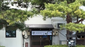 A building with a sign reading "Budget Room JINYA" and a traditional Japanese entrance gate. - Backpackers Jinya (Takayama)