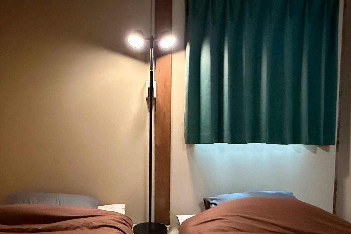 Ein Zimmer mit zwei Betten, einem Vorhangfenster und einer Stehlampe.