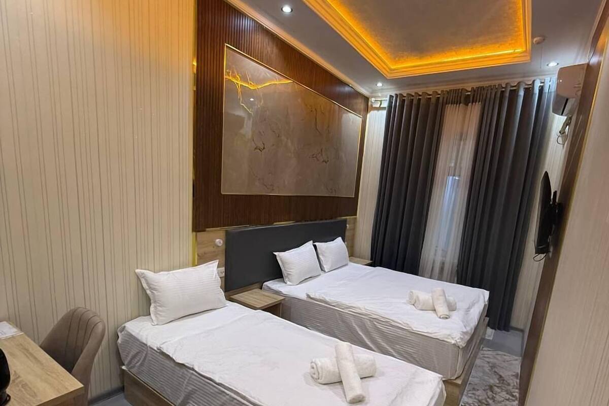 A hotel room with two beds, a desk, a chair, a large mirror, and a ceiling light fixture.