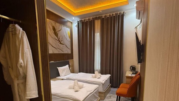 A hotel room with two beds, a robe rack, a desk with a chair, and a TV. - Safo Hotel (Tashkent)