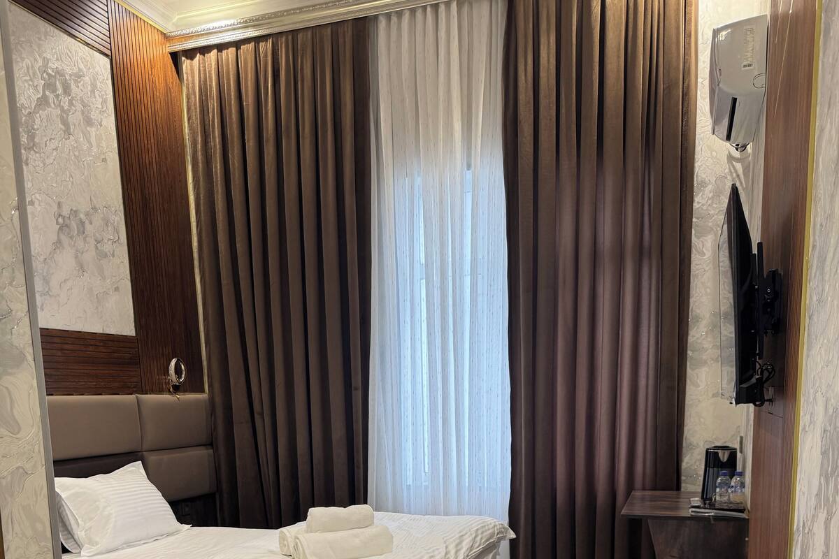 A modern hotel room with a large bed, a bedside table with a coffee maker, and a TV mounted on the wall.