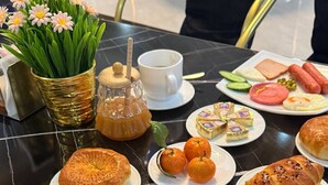 A breakfast table with plates of food, a coffee cup, and a flower vase. - Safo Hotel (Tashkent)