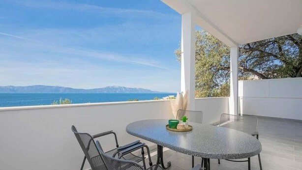 A balcony with a table and chairs, overlooking a coastal view with mountains in the distance. - Adriatic Serenity Haven (Gradac)