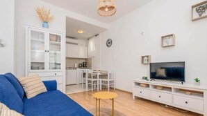 A modern living room with a blue sofa, a television, and a kitchen in the background. - Adriatic Serenity Haven (Gradac)