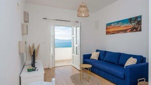 A room with a blue sofa, a small round table, a white desk, a hanging light fixture, and a painting of a sunset. - Adriatic Serenity Haven (Gradac)