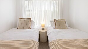 Une chambre avec deux lits, une table de chevet avec une lampe, des rideaux légers et une vue par la fenêtre.