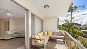 Un balcon avec un canapé, un ventilateur de plafond et une vue sur les palmiers.