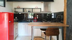 Una cocina compacta con un refrigerador rojo, una mesa de madera y una sola silla.