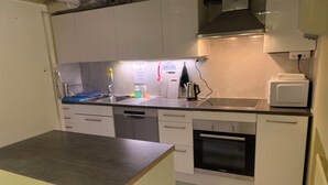 Ett kompakt kök med vita skåp, en inbyggd ugn, en mikrovågsugn och ett diskho.