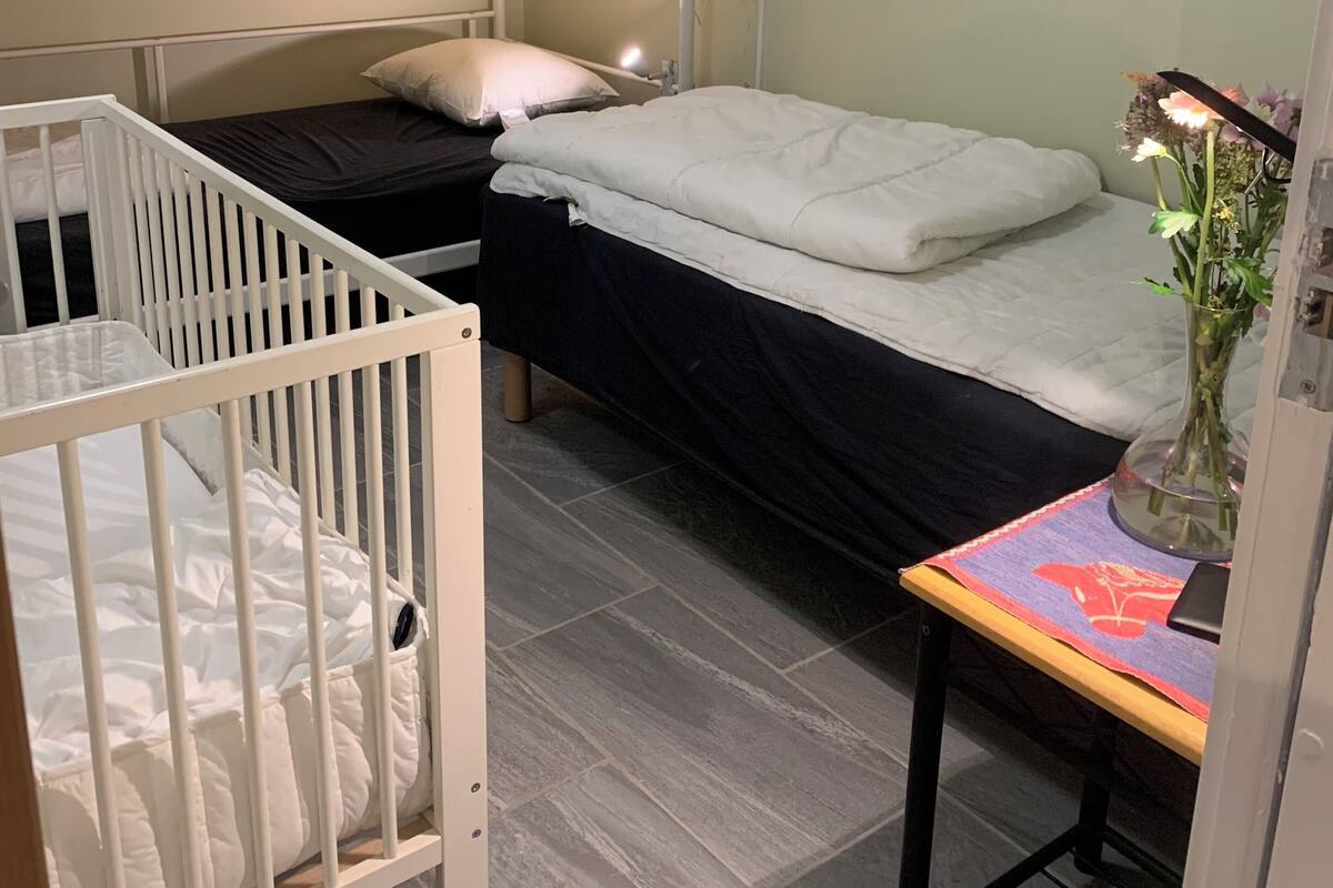 A bunk bed room with a crib, a bedside table with a vase, and a painting on the wall.
