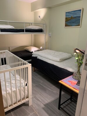 Une chambre avec un lit superposé, un berceau, une table de chevet avec un vase et un tableau au mur.