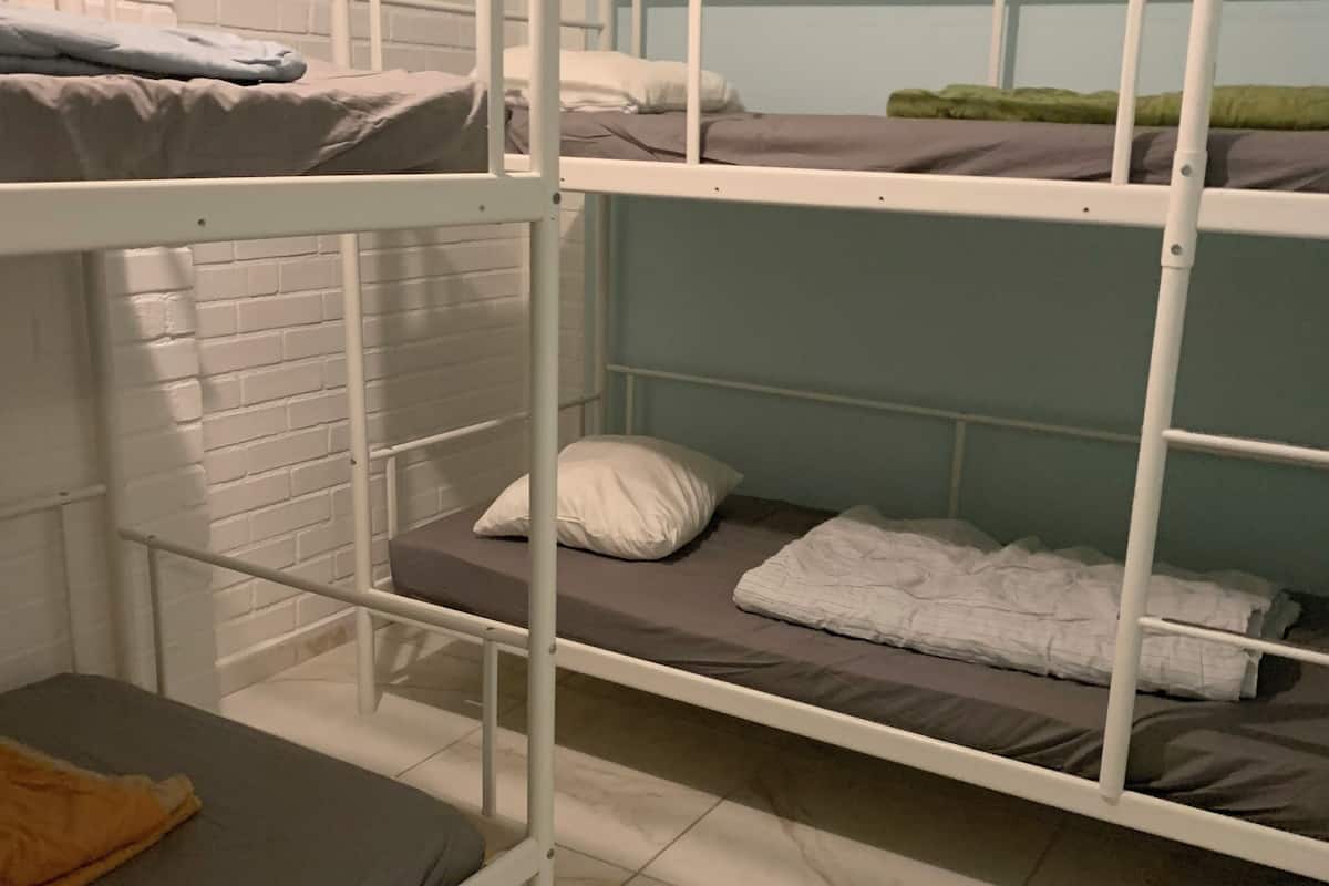A bunk bed room with white metal railings, grey mattresses, and a tiled floor.
