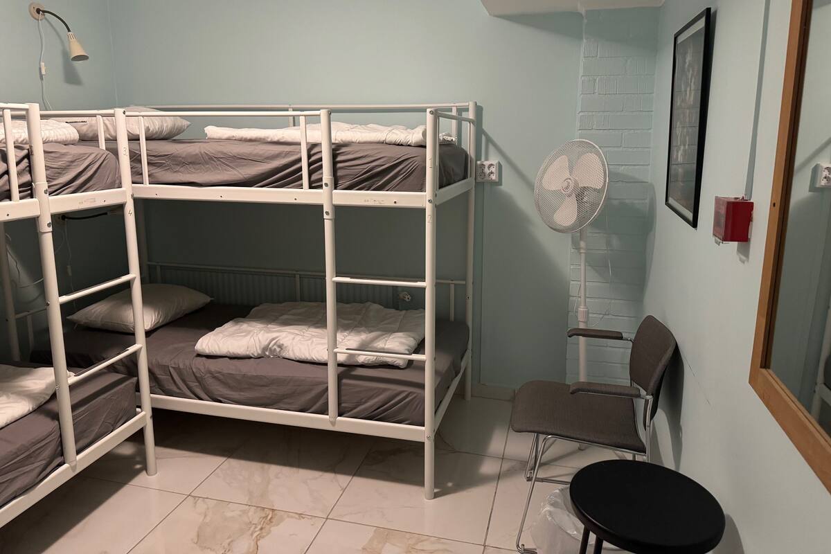 A bunk bed room with a desk, chair, and a standing fan.